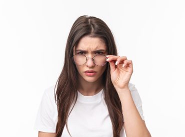 Close-up portrait of suspicious young serious-looking woman, look from under glasses, squinting at person with judgemental disbelief stare, standing white background, have doubts vision Problem